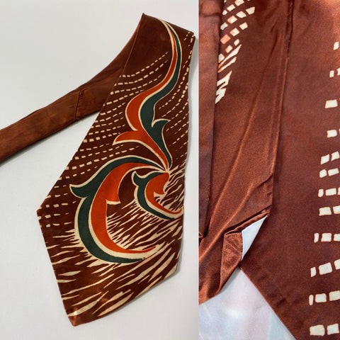 1940s US swing tie in red clay brown with orange, green and white abstract pattern. Open backs and short blade at 123cm long 11cm wide. No damage.